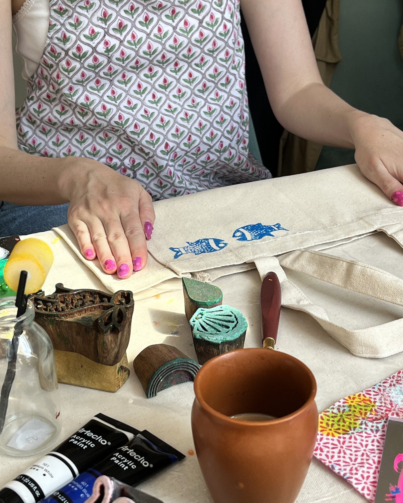 Hands stamping a small blue fish onto a tote