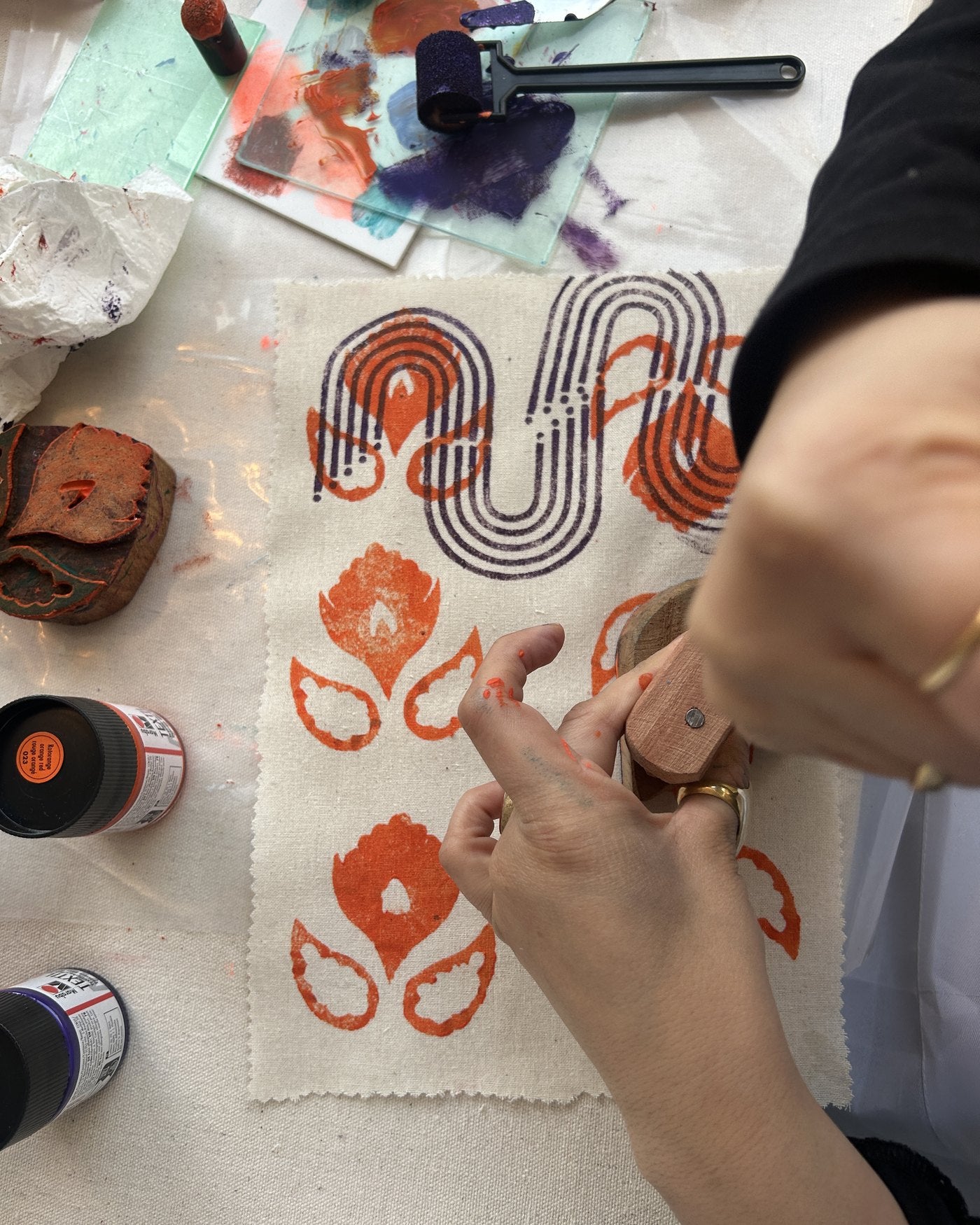 Hands stamping orange motifs onto fabric