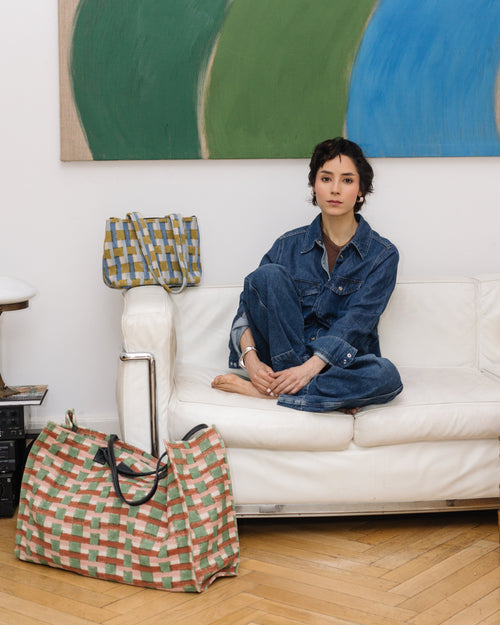 Woman sitting on a white couch with a colorful bag next to her in a room with abstract art on the wall.