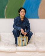 Person sitting on a white couch holding a colorful bag, with a abstract painting in the background.