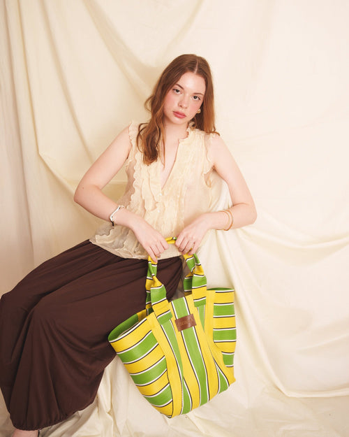 Woman holding a green and yellow striped bag against a plain background