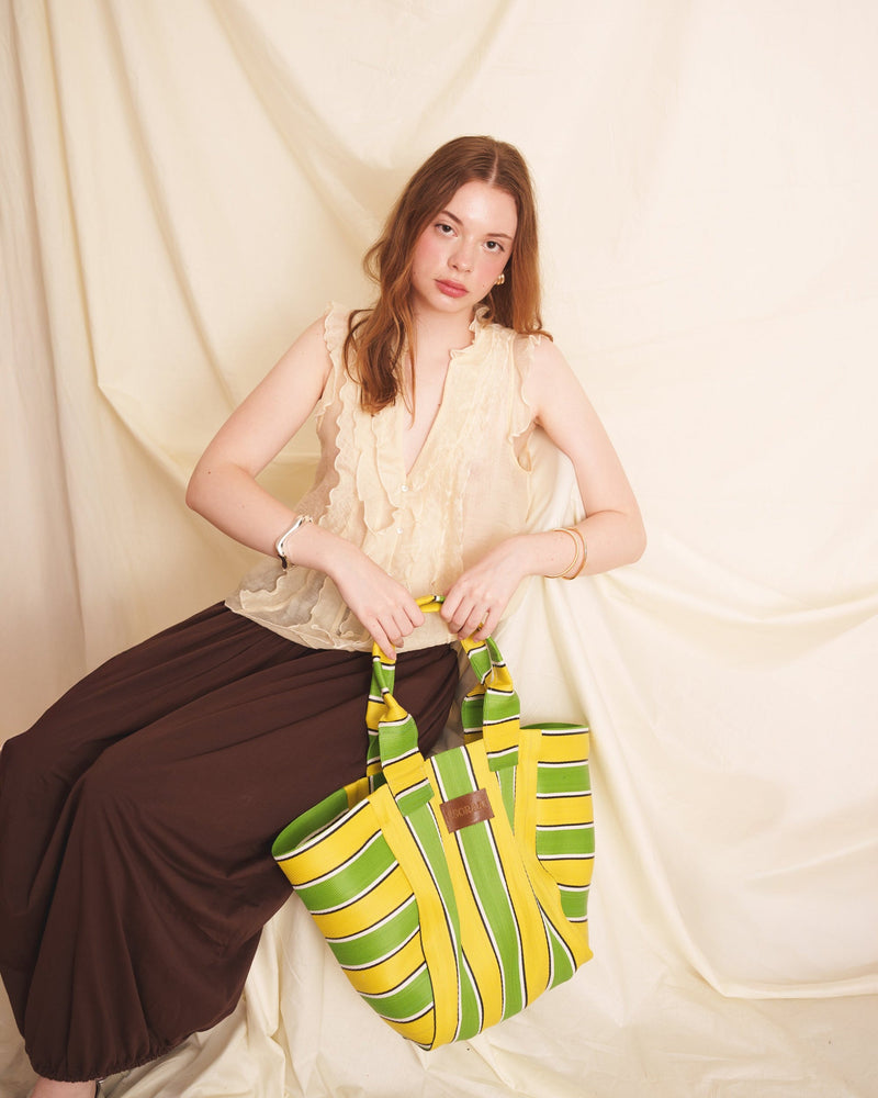 Woman holding a green and yellow striped bag against a plain background