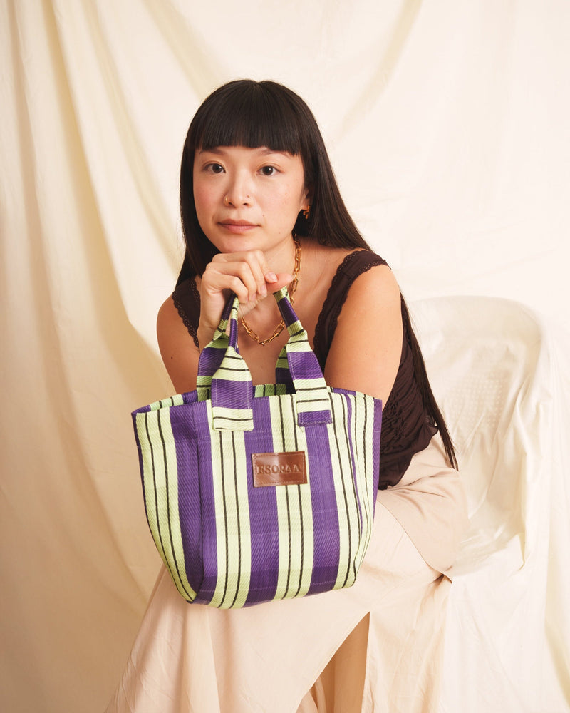 Woman holding a striped handbag against a plain background