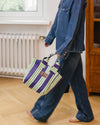 Person wearing a denim jacket and jeans holding a striped bag indoors.