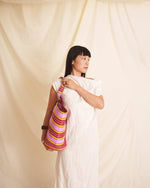 Woman holding a pink colorful bag against a plain background