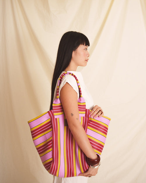 Woman holding a pink striped bag against a beige curtain