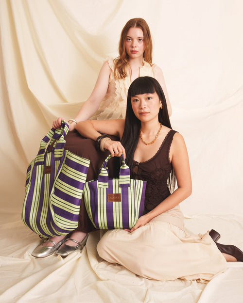 Two women holding striped bags against a plain background