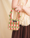 Person holding an orange checkered sustainable bag against a beige background