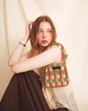 Woman wearing an orange checkered  mini purse on her shoulder against a plain background