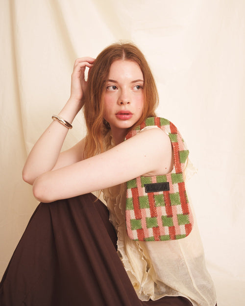 Woman wearing an orange checkered  mini purse on her shoulder against a plain background