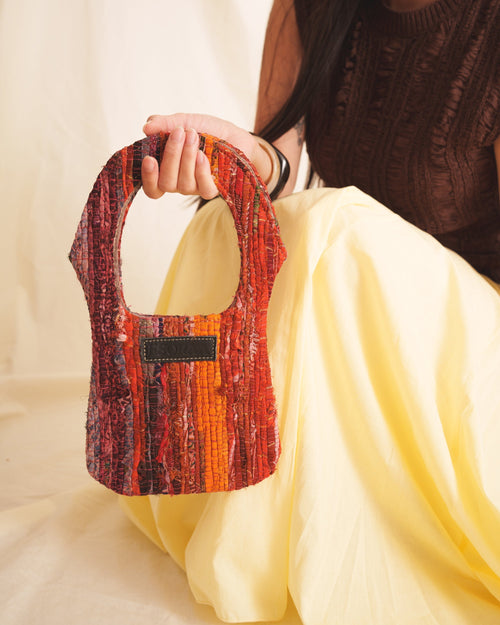 Person holding a small, colorful handbag with a plain background