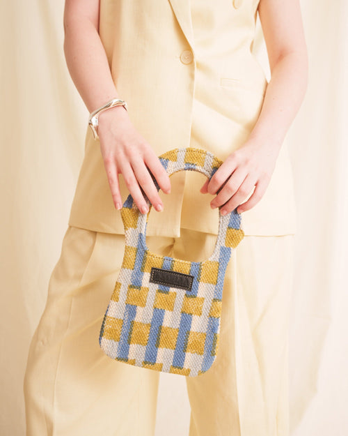 Person holding a small blue checkered bag against a beige background