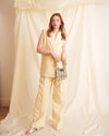 Woman in a yellow outfit holding a blue and white checkered bag against a draped fabric background