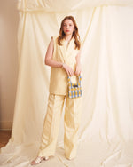 Woman in a yellow outfit holding a blue and white checkered bag against a draped fabric background