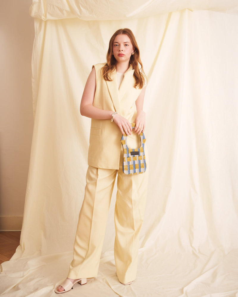 Woman in a yellow outfit holding a blue and white checkered bag against a draped fabric background