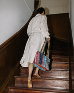 Person in a white coat ascending a wooden staircase with a colorful bag.