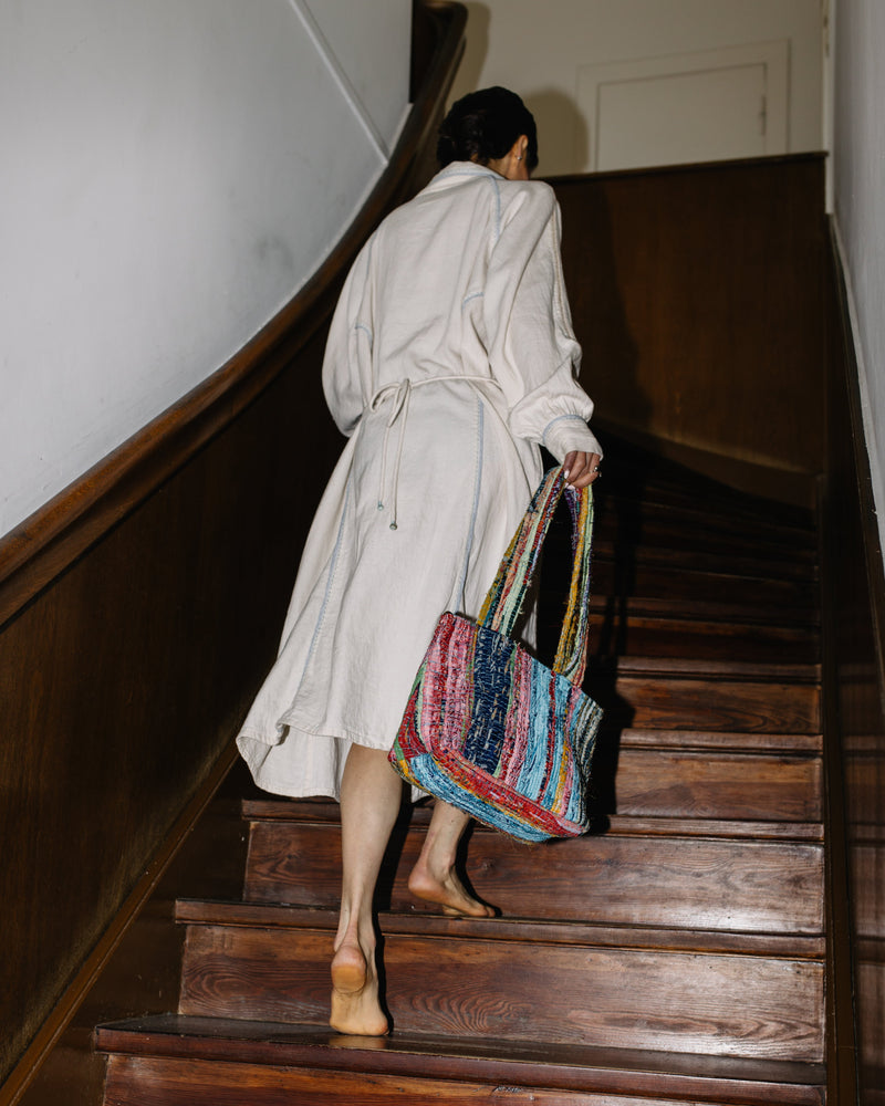 Person in a white coat ascending a wooden staircase with a colorful bag.