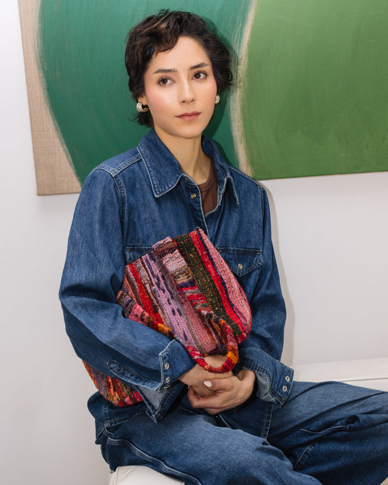 Person wearing a denim jacket holding a colorful bag against a green abstract painting.