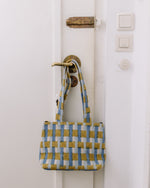 Handbag with blue and yellow checkered pattern hanging on a white door handle.