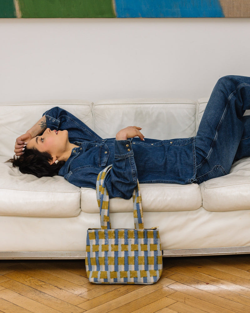 Person lying on a white couch with a checkered bag beside them, in a room with a colorful abstract painting on the wall.