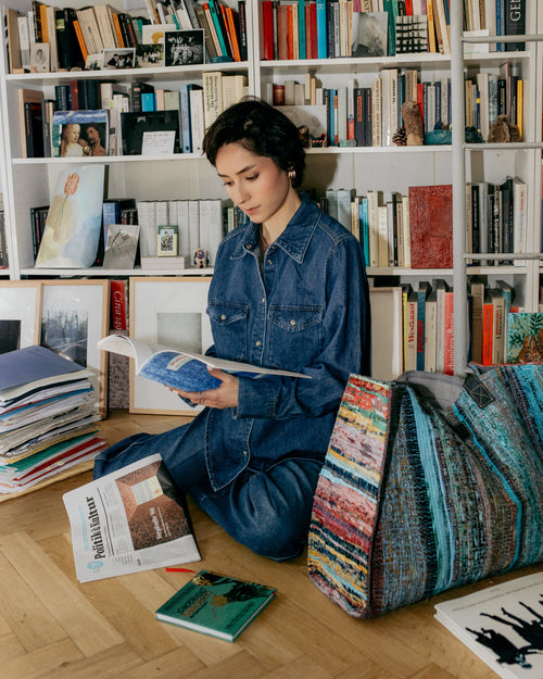 Woman reading a book on the floor in front of a bookshelf