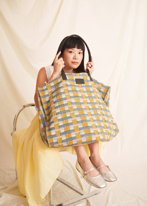 Woman holding a yellow and blue checkered handmade premium bag against a plain background