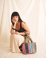 Woman holding a colorful handbag against a plain background