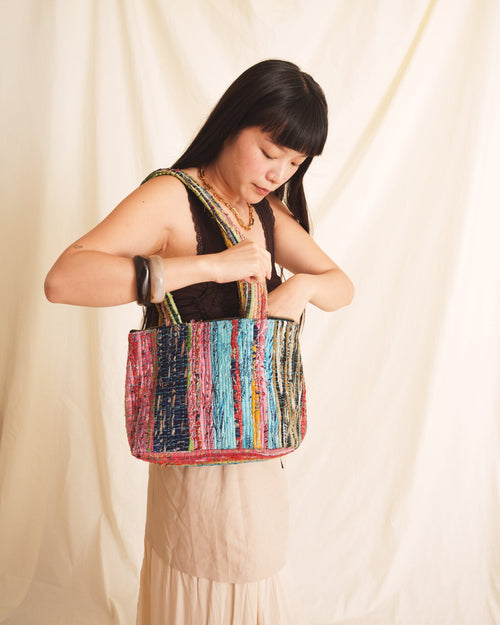 Woman holding a colorful blue striped bag against a plain background